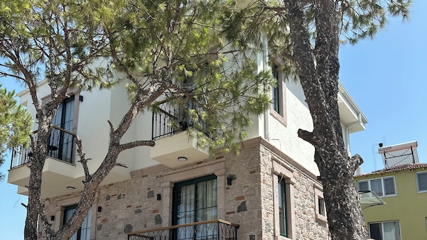 Un edificio de varios pisos con fachada de piedra y enlucido, balcones con barandillas de metal y un césped bien cuidado.