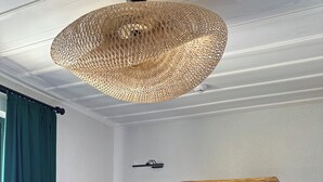 Una habitación de hotel con un escritorio de madera, un televisor, un armario y una lámpara de techo de mimbre.