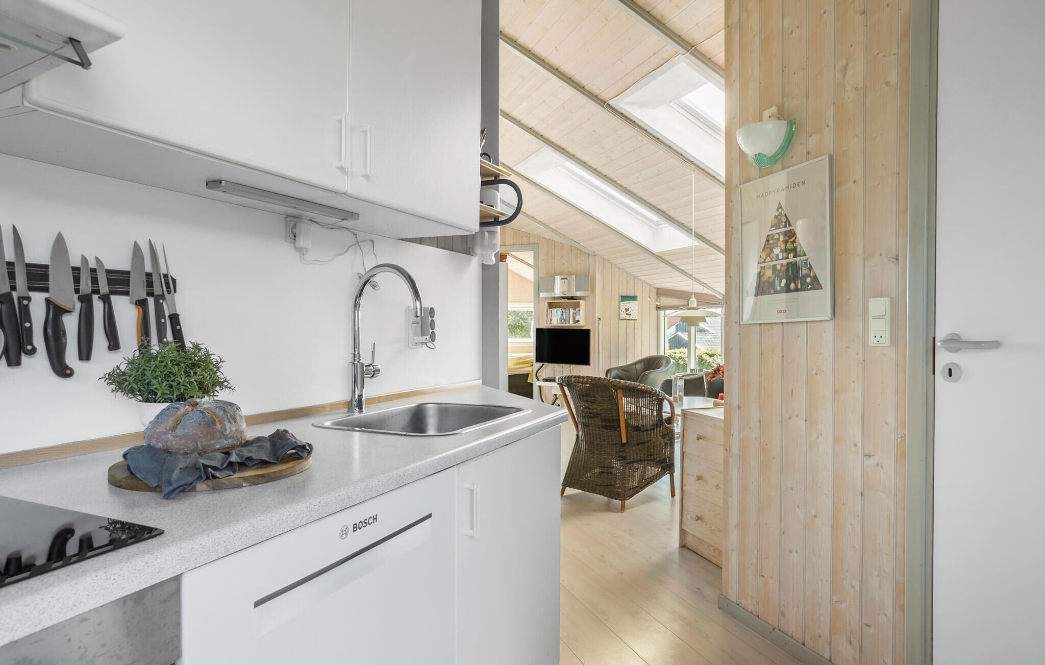 A modern kitchen with a Bosch dishwasher, a sink, and a variety of knives displayed on the wall.