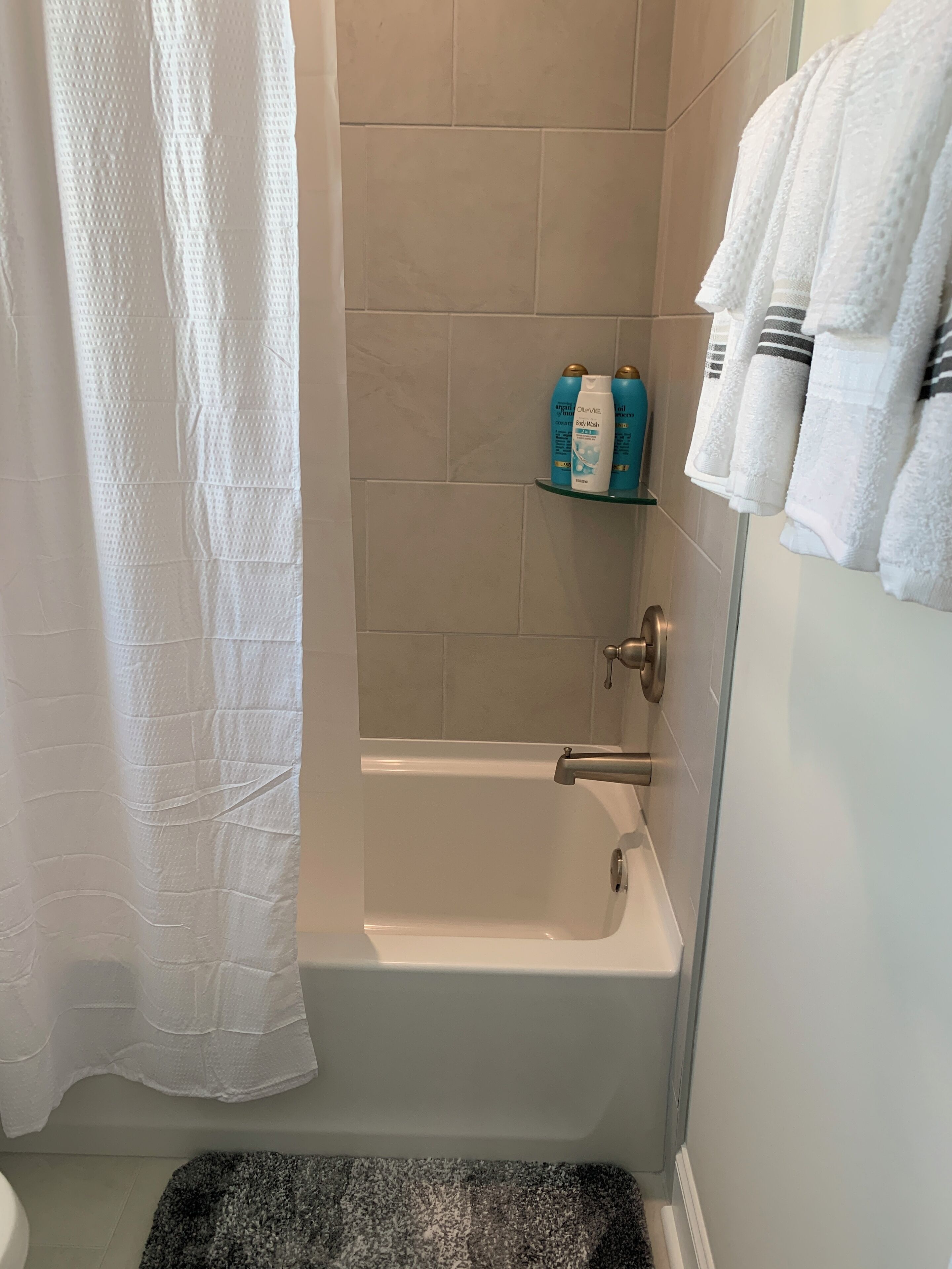 A bathroom with a bathtub, a shower curtain, a shelf with toiletries, and a rack of towels.