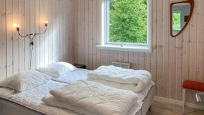 A bedroom with a bed, a bedside table, a nightstand, a window with a view of greenery, and a mirror on the wall.