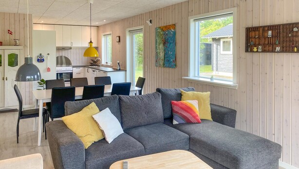 A modern living room with a grey sectional sofa, wooden coffee table, and a dining area with a white table and chairs.