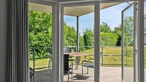 Ein überdachter Außenbereich mit Tisch und Stühlen, umgeben von Metallgeländern und Blick ins Grüne.