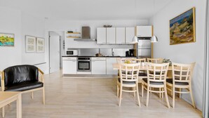 Eine moderne Küche mit weißen Schränken, einer Mikrowelle und einem Herd. Ein Essbereich mit Holzkohlen und einem Tisch ist vorhanden.