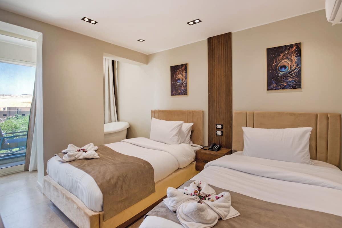 A hotel room with two beds, a large window, and artwork on the walls.