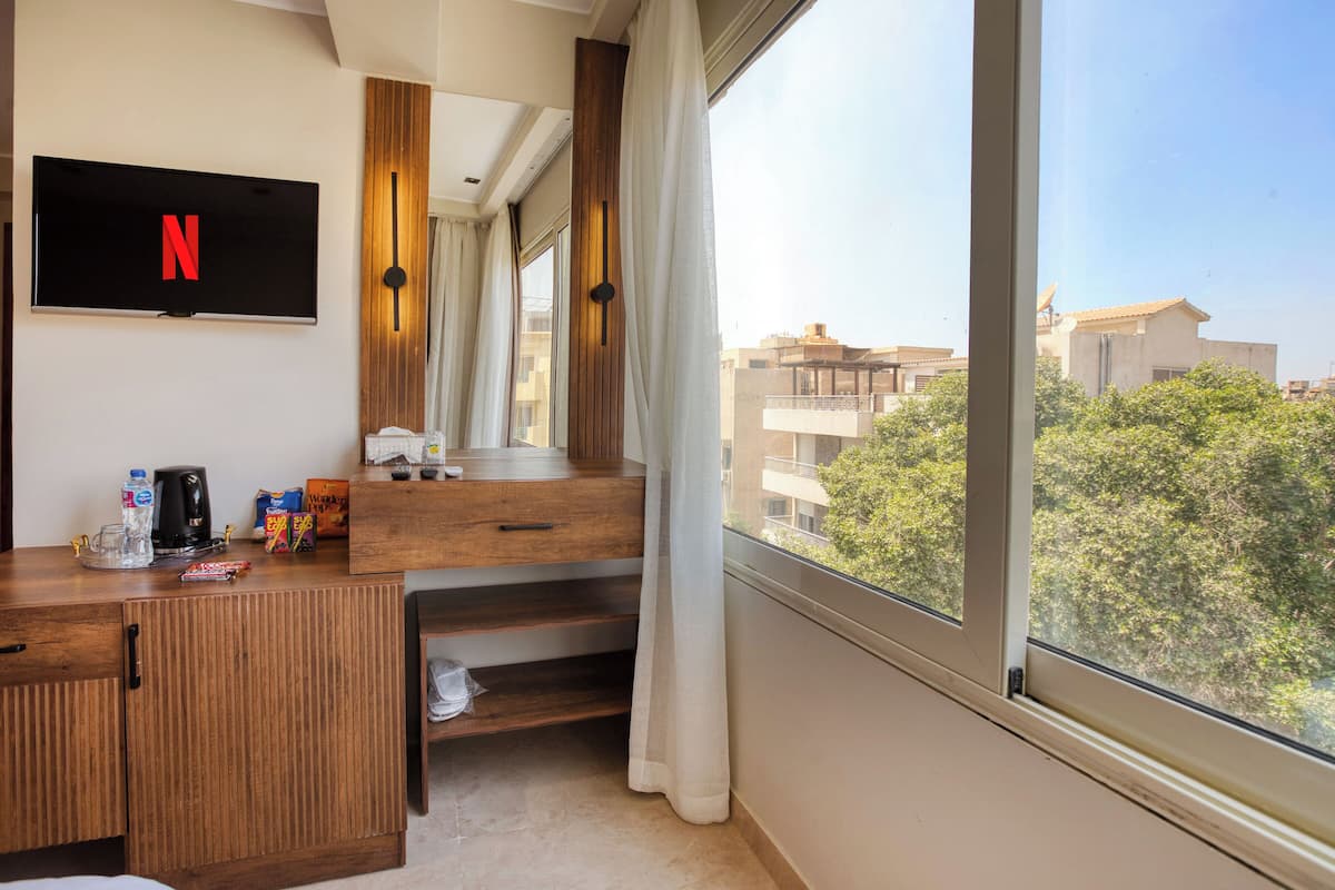 A hotel room with a large window, a flat-screen TV with the Netflix logo, a wooden desk, and a view of the cityscape.