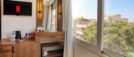 Une chambre d’hôtel dotée d’une grande fenêtre, d’un téléviseur à écran plat affichant le logo de Netflix, d’un bureau en bois et offrant une vue sur le paysage urbain.