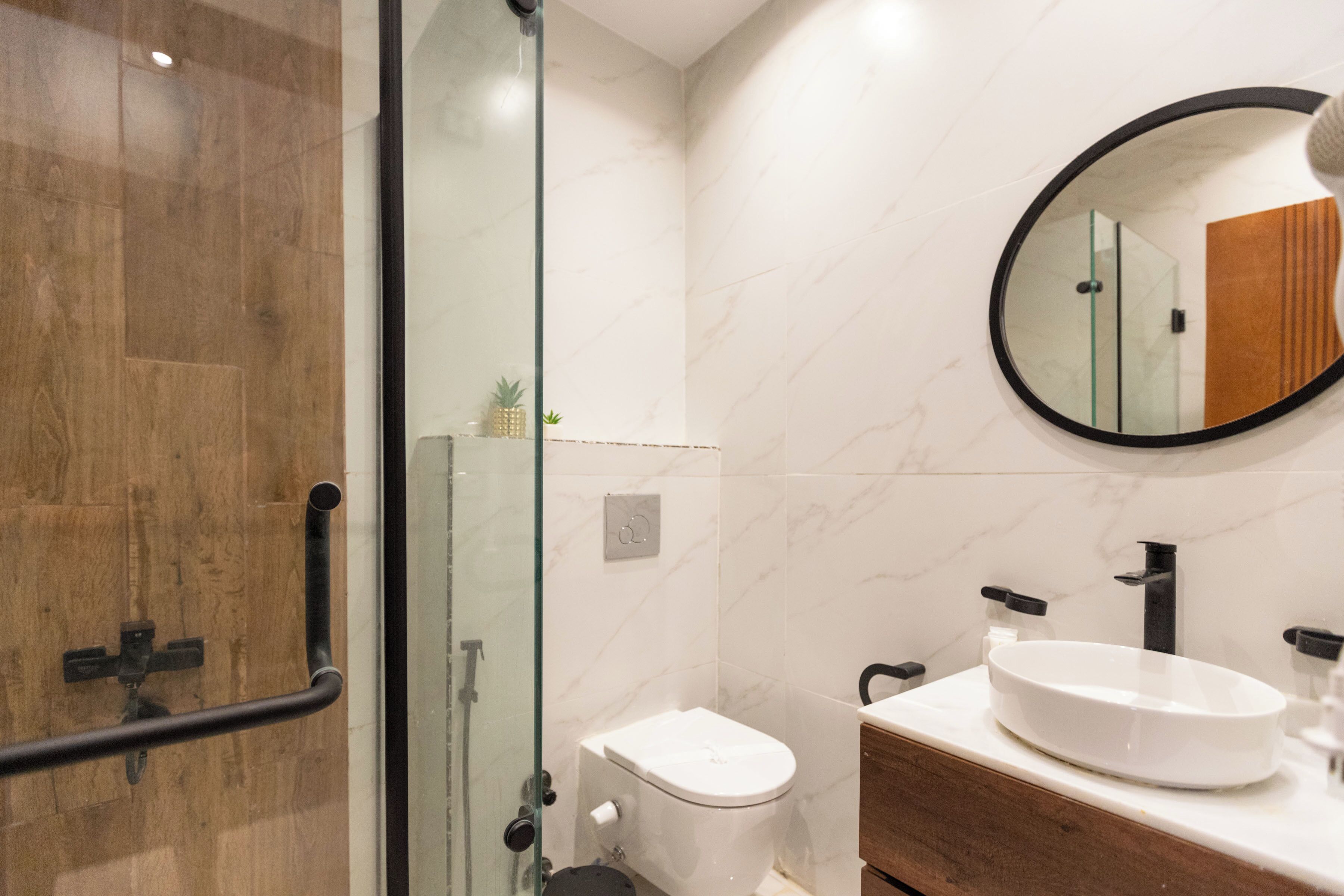Un bany modern amb una dutxa envidriada, un vàter blanc i un lavabo de fusta amb un rentapla blanc.