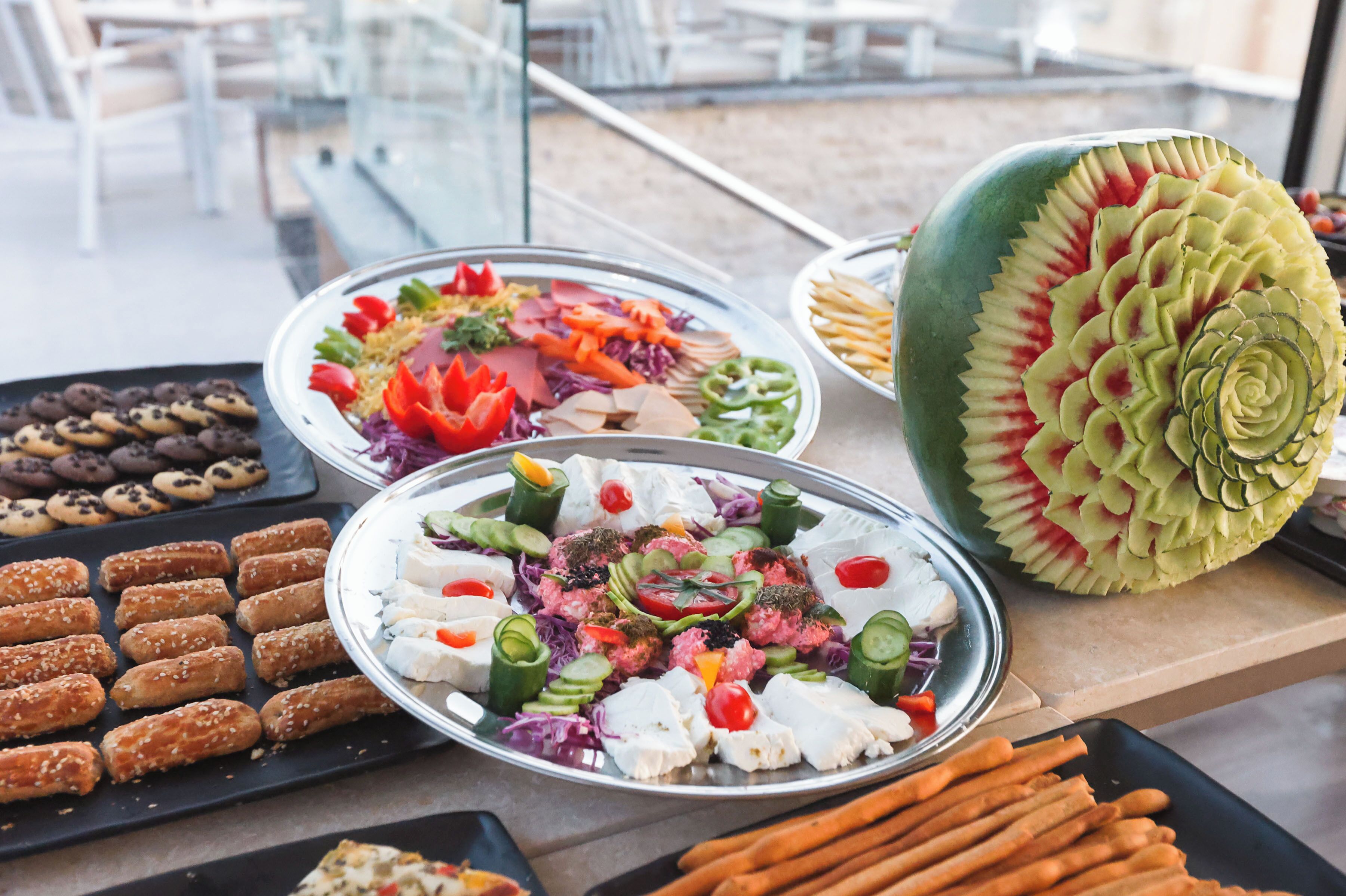 Un tavolo da buffet con diversi cibi, tra cui un'anguria intagliata a forma di fiore.