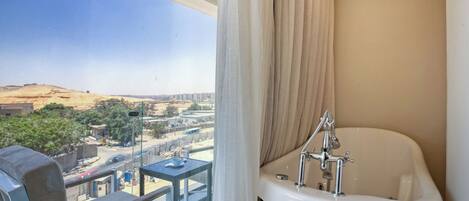 A balcony with a chair and table, a bathtub, and a view of a cityscape.