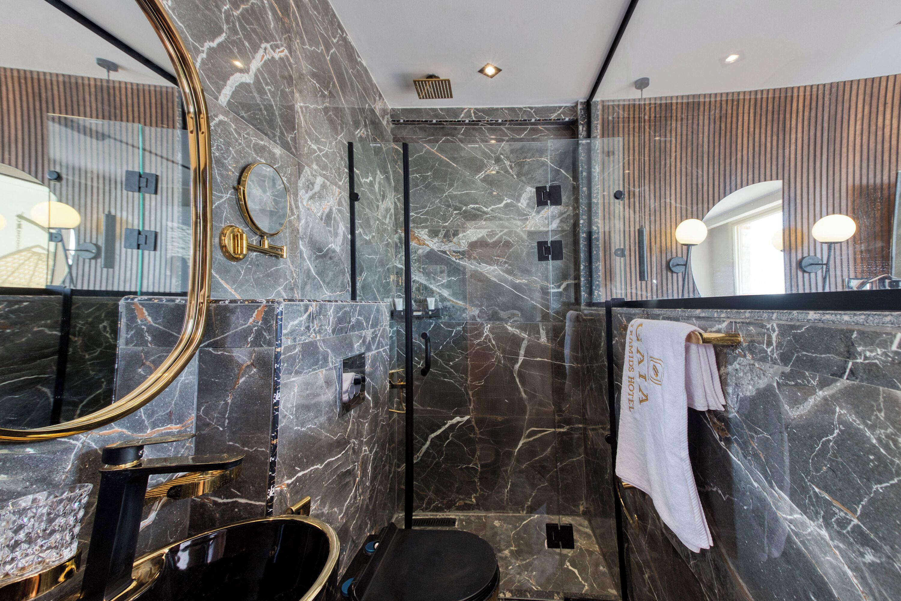 Un baño moderno con ducha de mármol, bañera negra y un espejo grande.