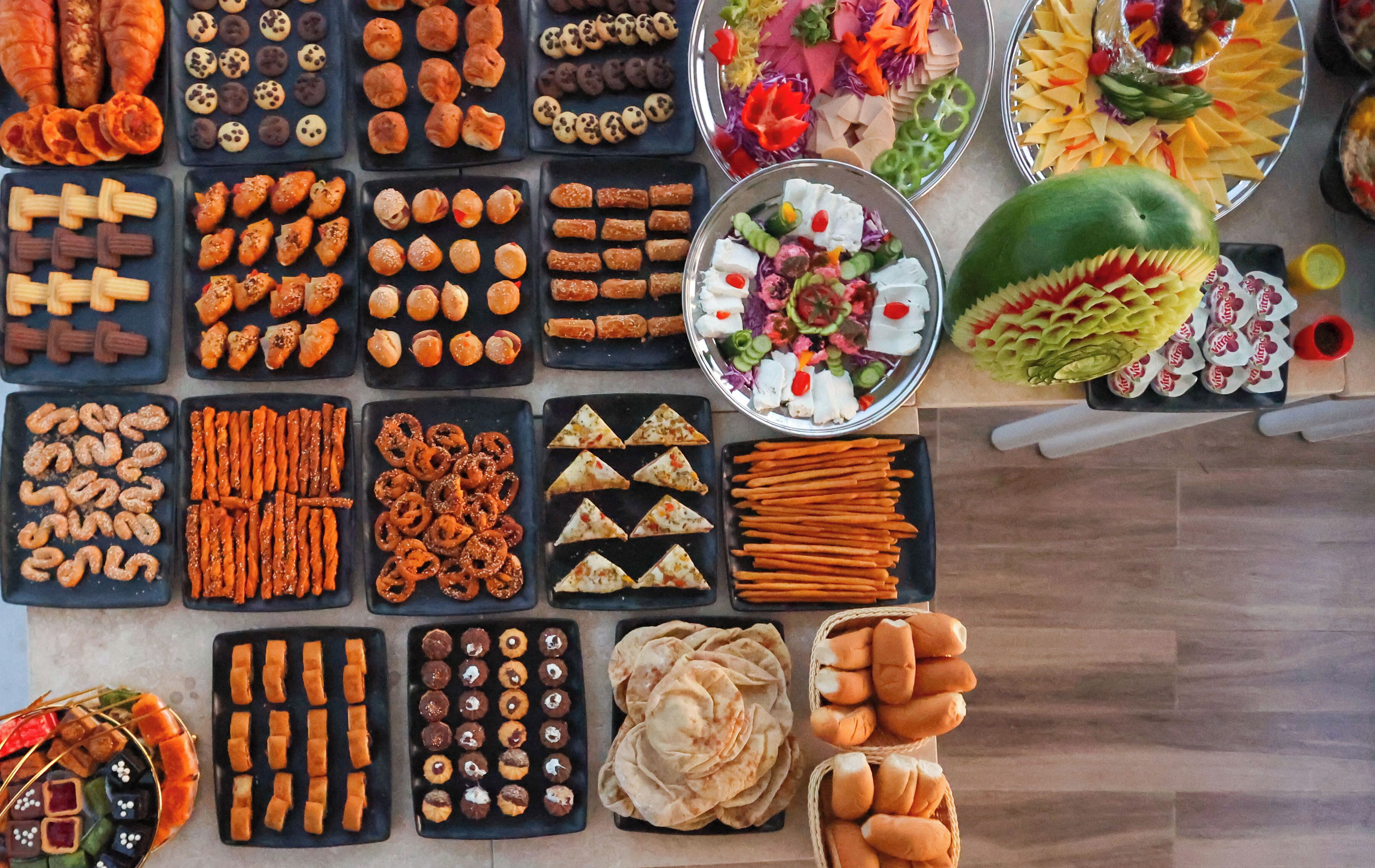 A variety of food items arranged on trays and plates, including pastries, snacks, and vegetables.