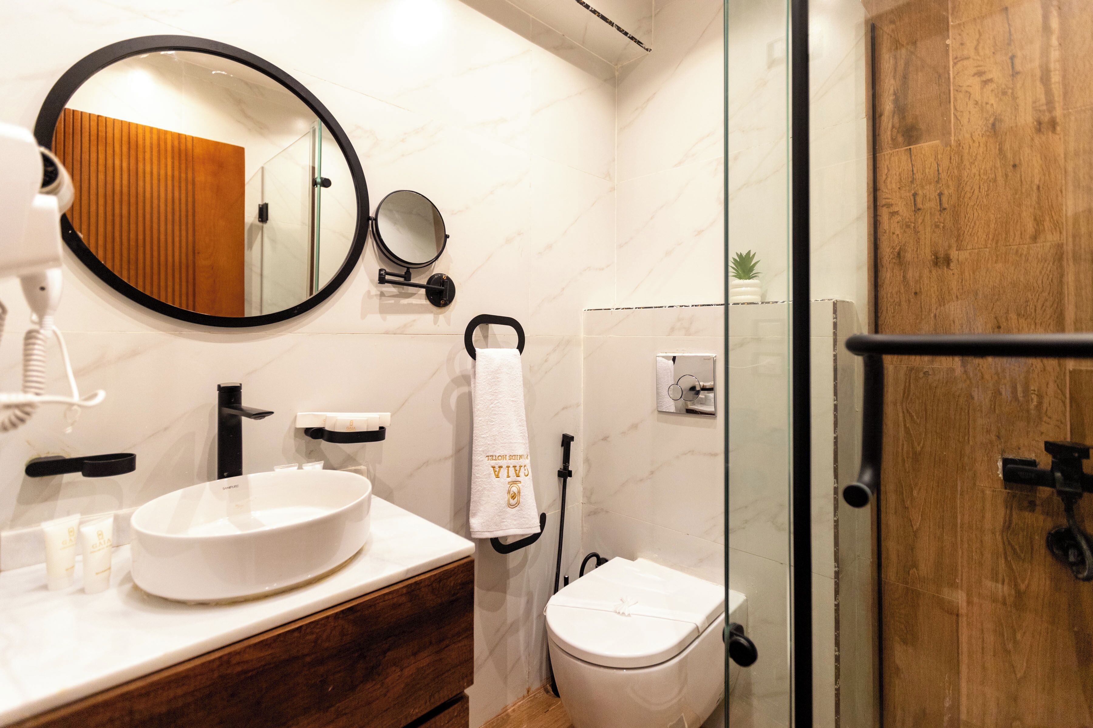 A bathroom with a round mirror, a sink, a toilet, and a glass shower enclosure.