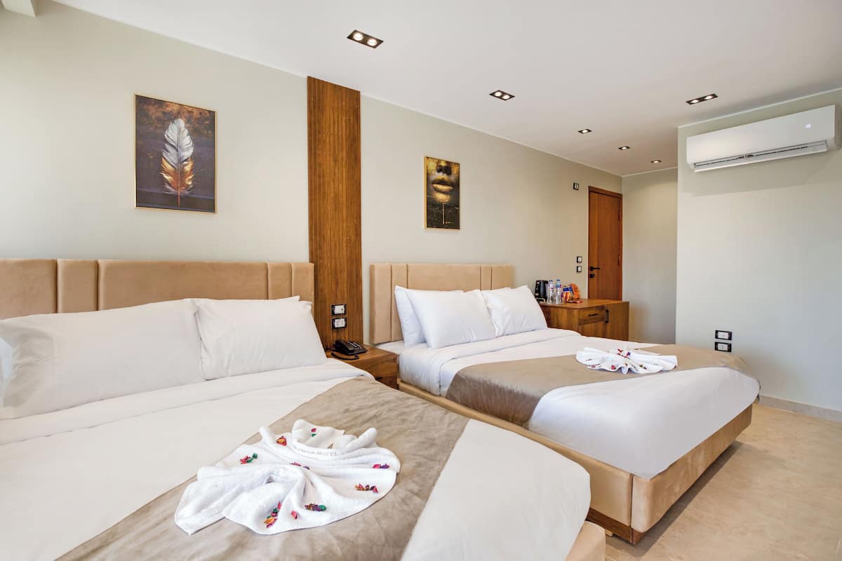 A hotel room with two beds, a wooden headboard, a wall-mounted air conditioner, and a painting above the beds.