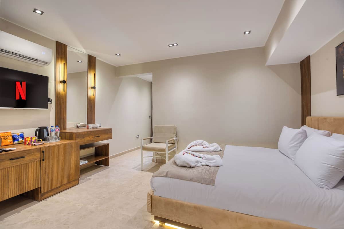 A modern hotel room with a large bed, a wooden vanity, a flat-screen TV, and a chair.