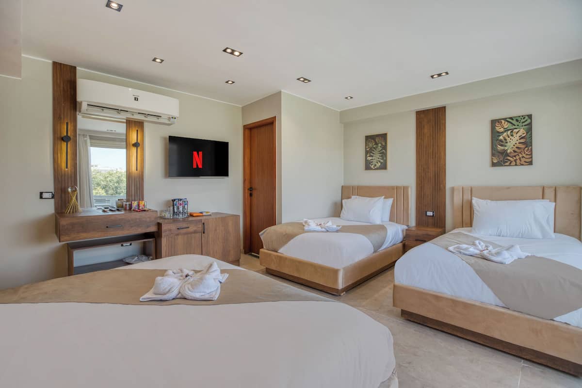 A hotel room with three beds, a TV, a minibar, and a large window.