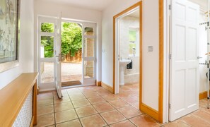 A hallway with a tiled floor leading to a bathroom with a sink and a door to a garden area. - Norwich Luxury Getaway With 4 Bedrooms & Annex (Norwich)