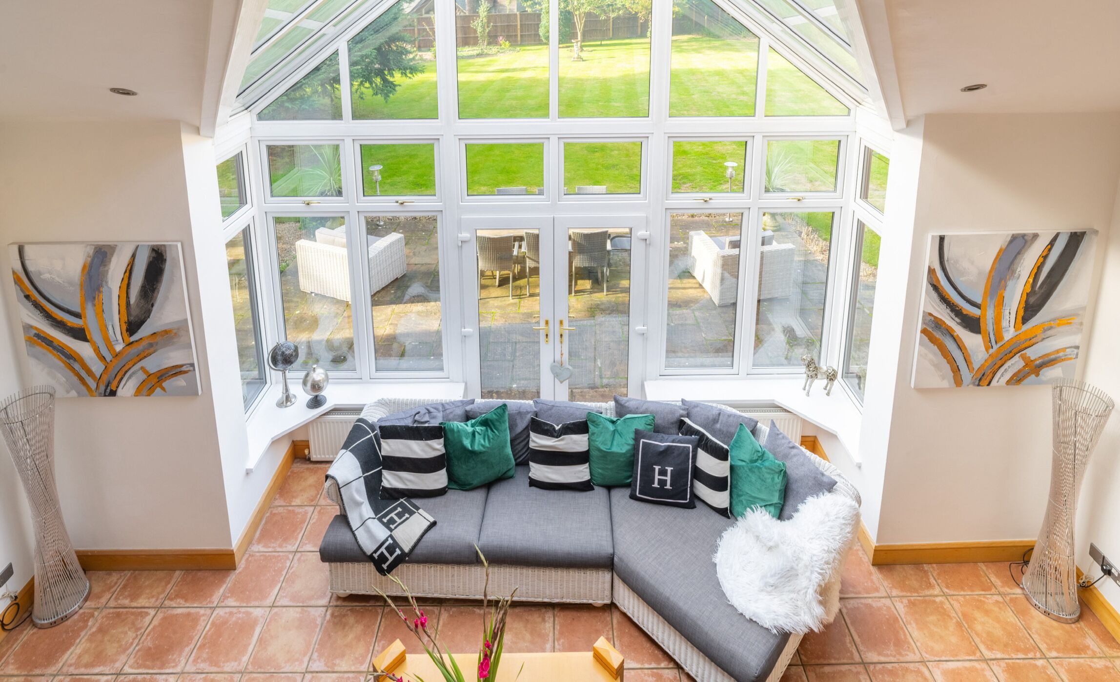 A cozy room with a large window overlooking a garden, a comfortable sofa with cushions, and two abstract paintings on the walls.