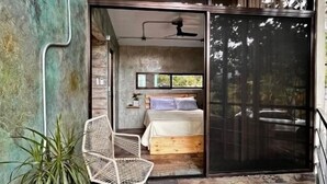 Una camera da letto moderna con un letto, una ventola a soffitto e un'ampia porta scorrevole in vetro che dà su un balcone.