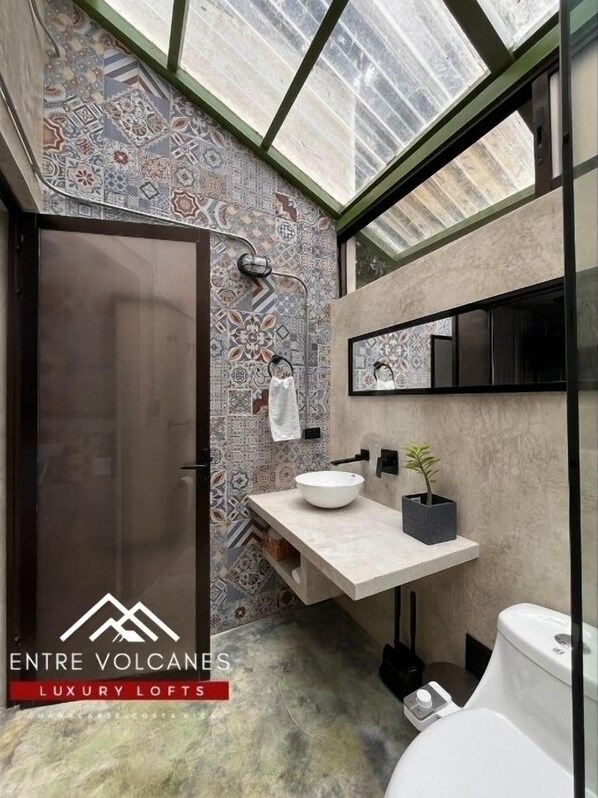 A bathroom with a skylight, patterned tiles, a large mirror, a sink with a bowl, and a toilet. - Apartamento con Vista al Volcán (Rio Naranjo)