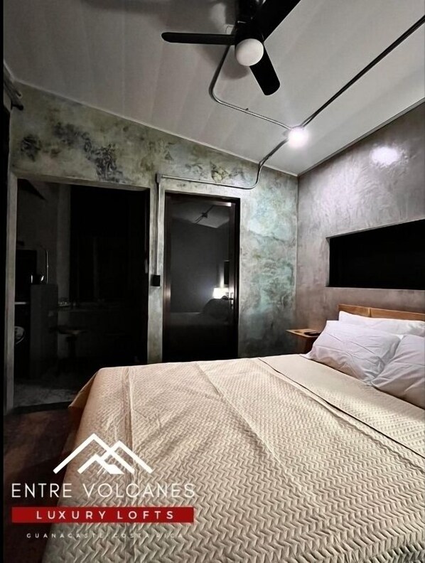 A bedroom with a bed, a ceiling fan, and a door leading to a bathroom. - Apartamento con Vista al Volcán (Rio Naranjo)