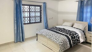 A bedroom with a bed, curtains, an air conditioning unit, a ceiling fan, and a window with a metal grille. - Serenity Retreat in Ashongman Estate (North Legon)