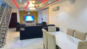 A modern living room with a TV, sofa, and dining area. - Serenity Retreat in Ashongman Estate (North Legon)