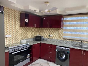 A compact kitchen with a stove, microwave, and washing machine. - Serenity Retreat in Ashongman Estate (North Legon)