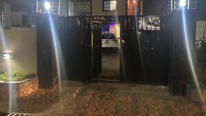 A gated entrance with a car parked inside, a tiled pathway leading to the gate, and a building with a window in the background. - Serenity Retreat in Ashongman Estate (North Legon)