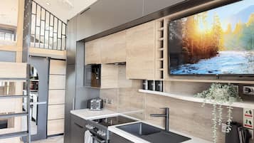 Una cocina moderna con horno empotrado, microondas, lavamanos y un televisor de pantalla plana que muestra una escena de bosque.