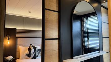 A modern bedroom with a bed, bedside table, lamp, and a large mirror.