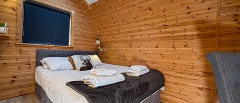 Une chambre confortable dans un chalet en bois, avec une lucarne, un lit orné d’un coussin à motif de cerf et une table de chevet avec une lampe.