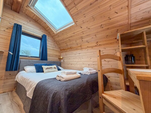 A cozy wooden room with a bed, a desk, and a skylight.