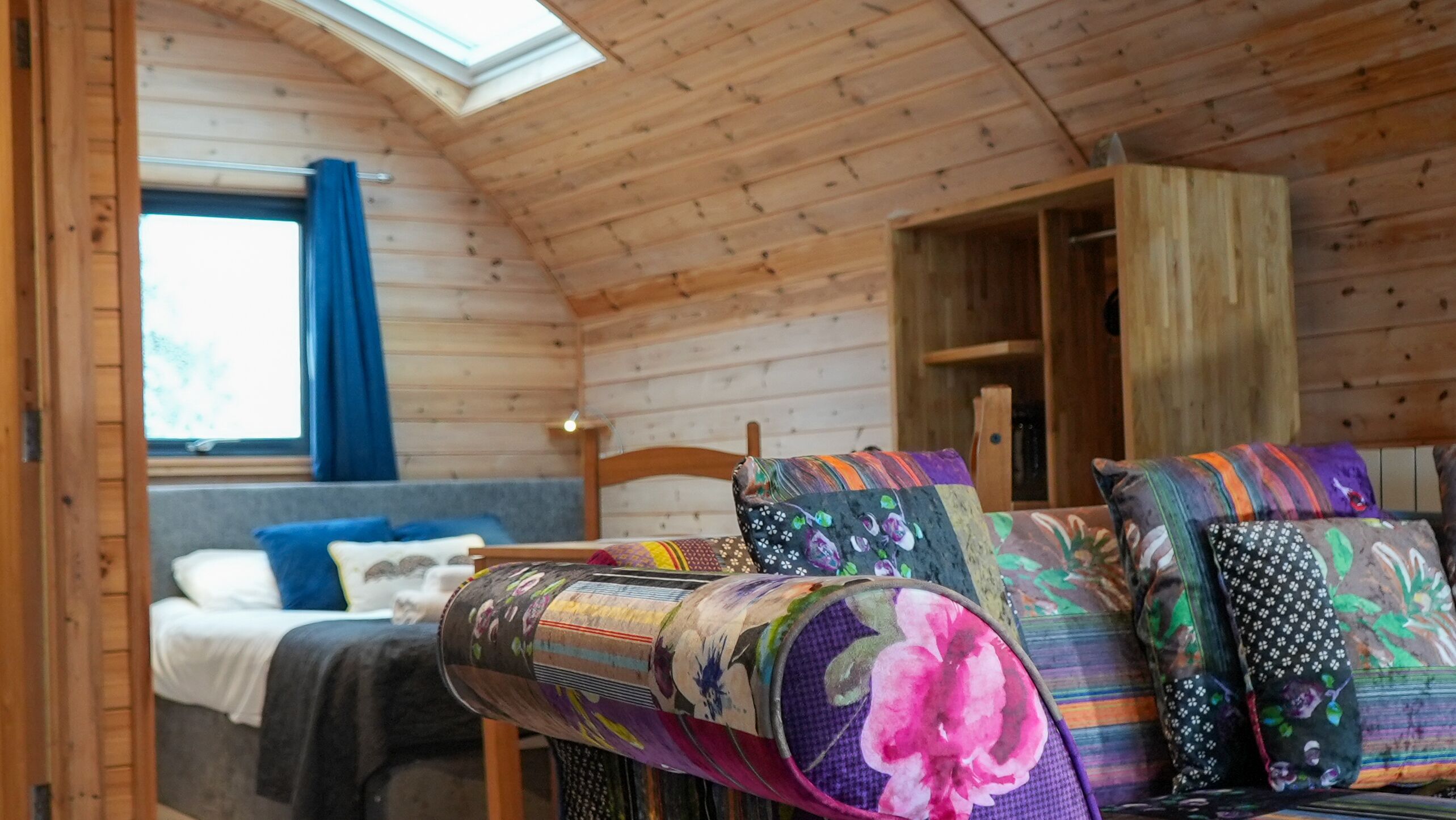 A cozy cabin interior with a loft bed, a wooden ceiling, and a skylight.