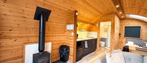 Un interior de cabaña acogedor con estufa de leña, kitchenette, baño y zona de estar.