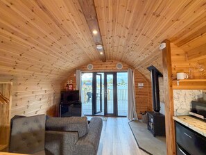 L’intérieur chaleureux d’un chalet, avec un plafond en bois, un canapé, un coin cuisine et une vue à travers les portes vitrées.