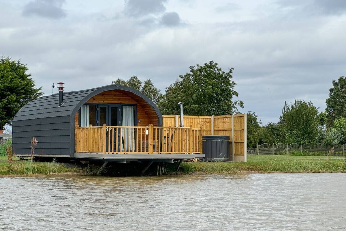 Et flydende hus med træterrasse og stort vindue, beliggende i vandet.