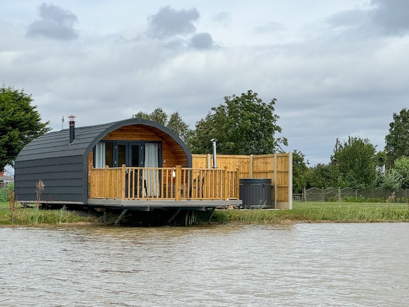 Une maison flottante dotée d’une terrasse en bois et d’une grande fenêtre, située sur une étendue d’eau.