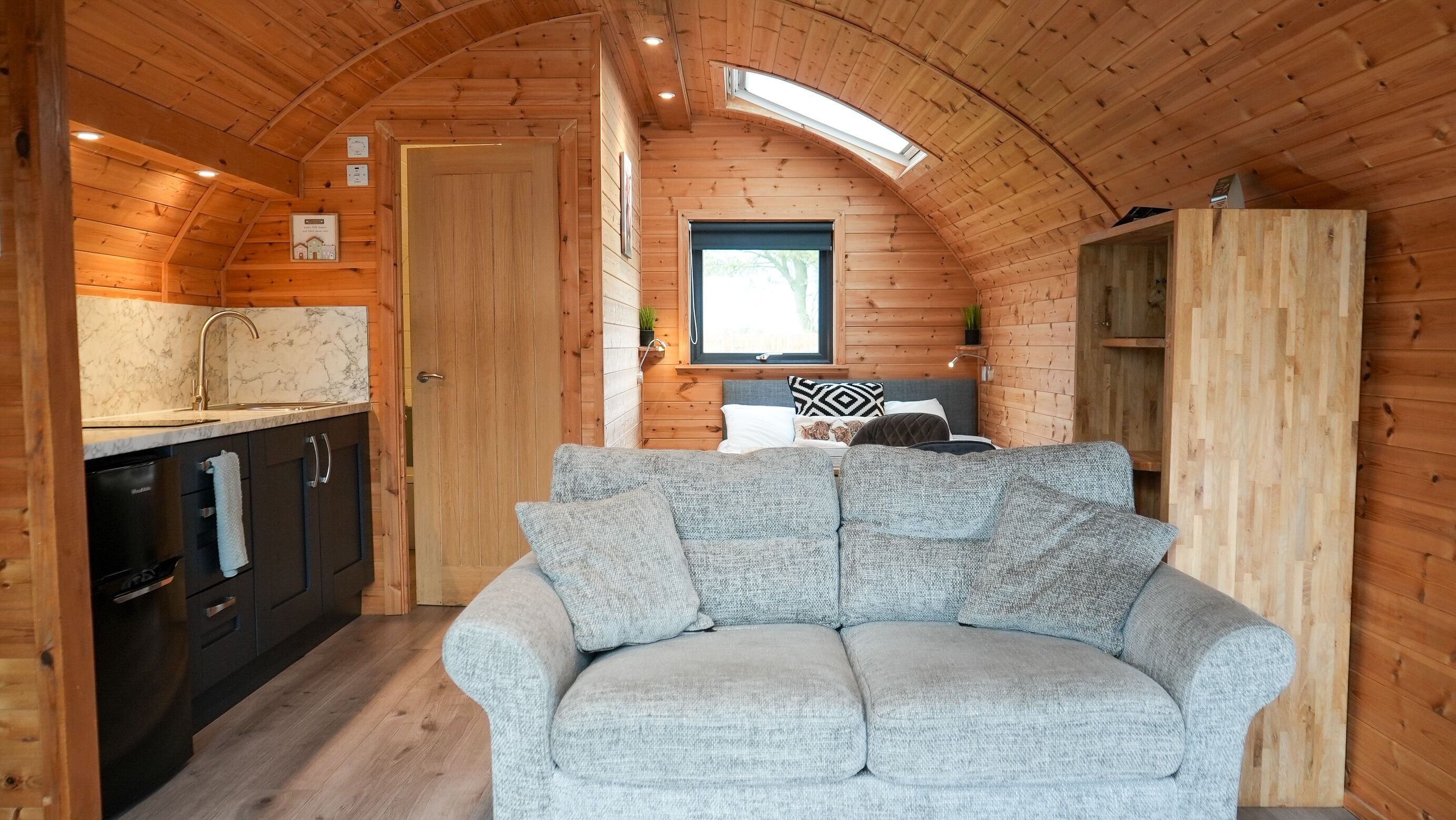 Interior acogedor de una cabaña con techo de madera, un sofá, zona de comedor y una ventana.