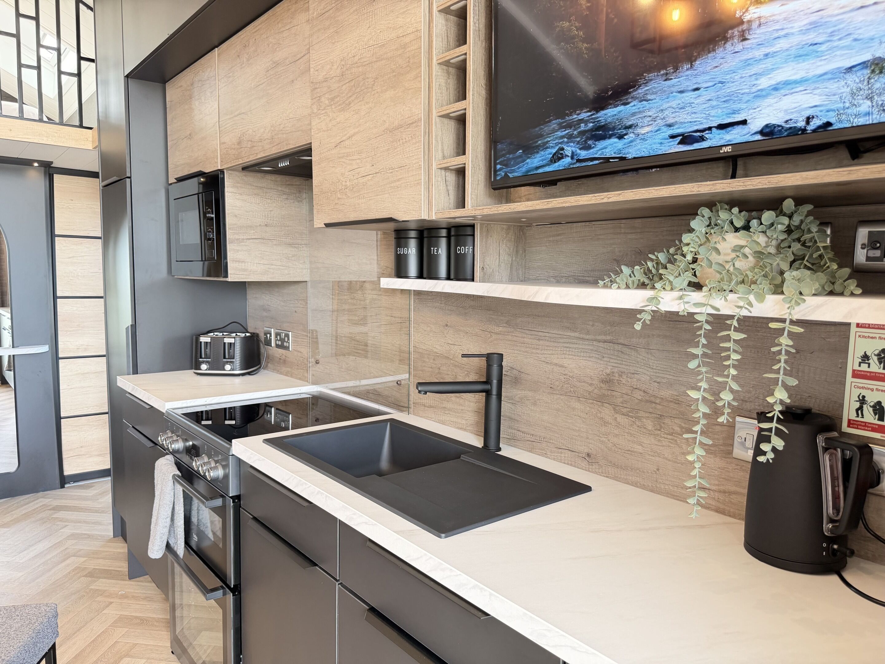 A modern kitchen with a built-in stove, a sink, and a flat-screen TV mounted above the counter.