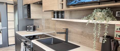 A modern kitchen with a built-in stove, a sink, and a flat-screen TV mounted above the counter.