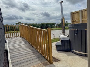 Une terrasse en bois menant à un espace barbecue équipé d’une cheminée et d’un jacuzzi.