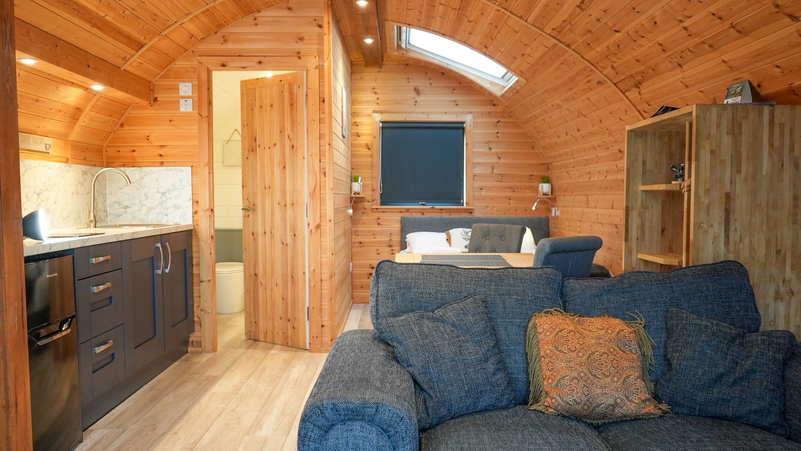 A cozy cabin interior with a wooden interior, a sofa, a dining table, and a kitchen area.