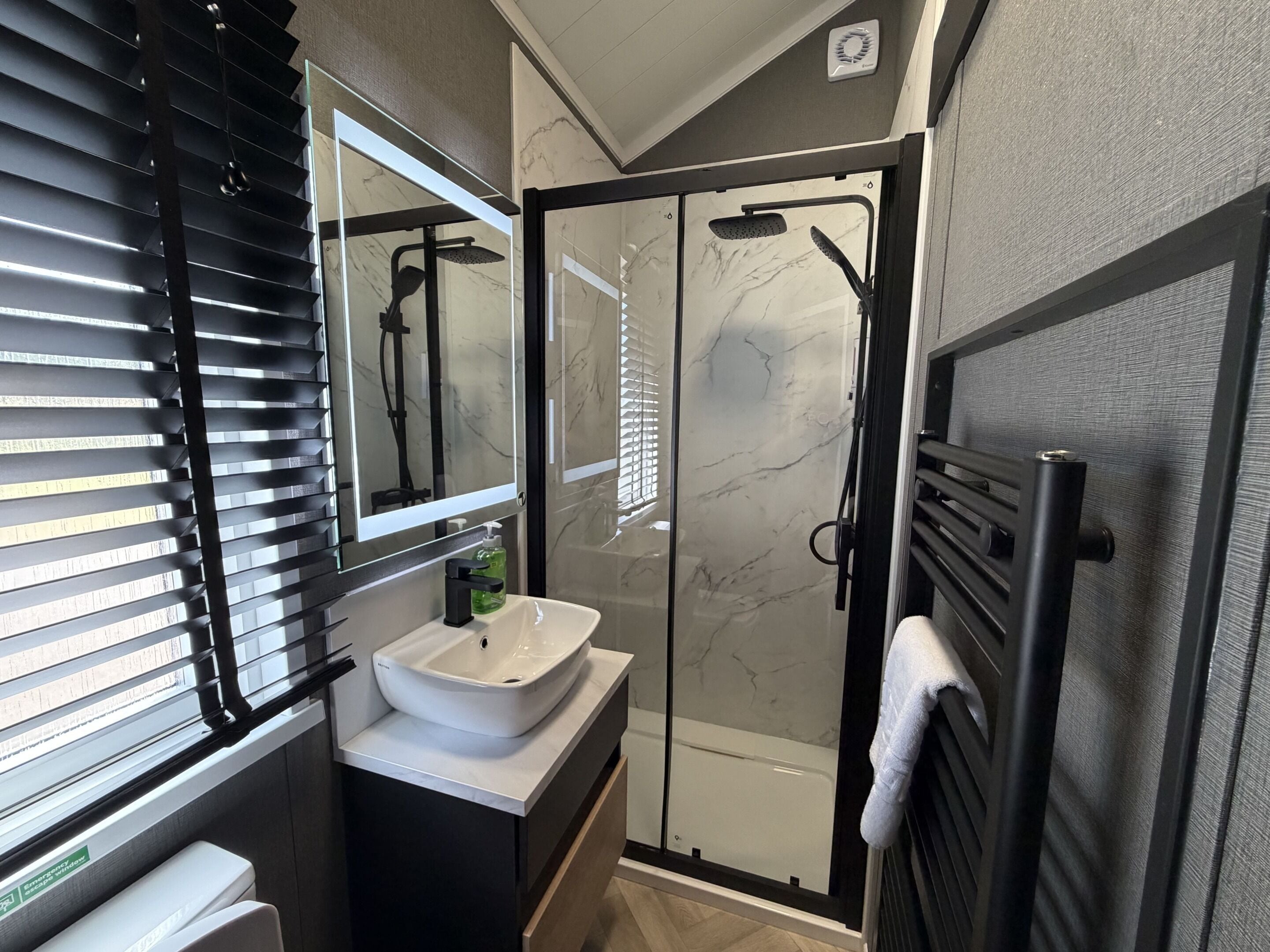 A modern bathroom with a glass-enclosed shower, a white sink, and a towel rack.
