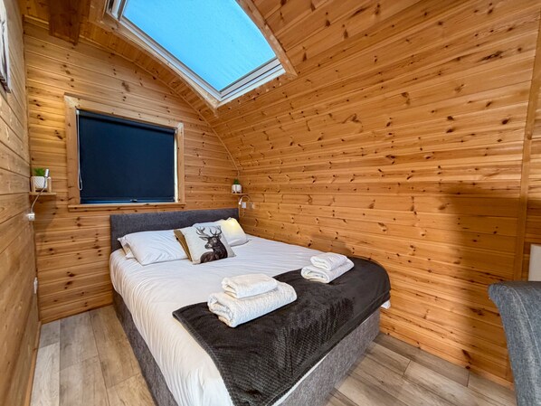 Una habitación acogedora de madera con cama, tragaluz y ventana.