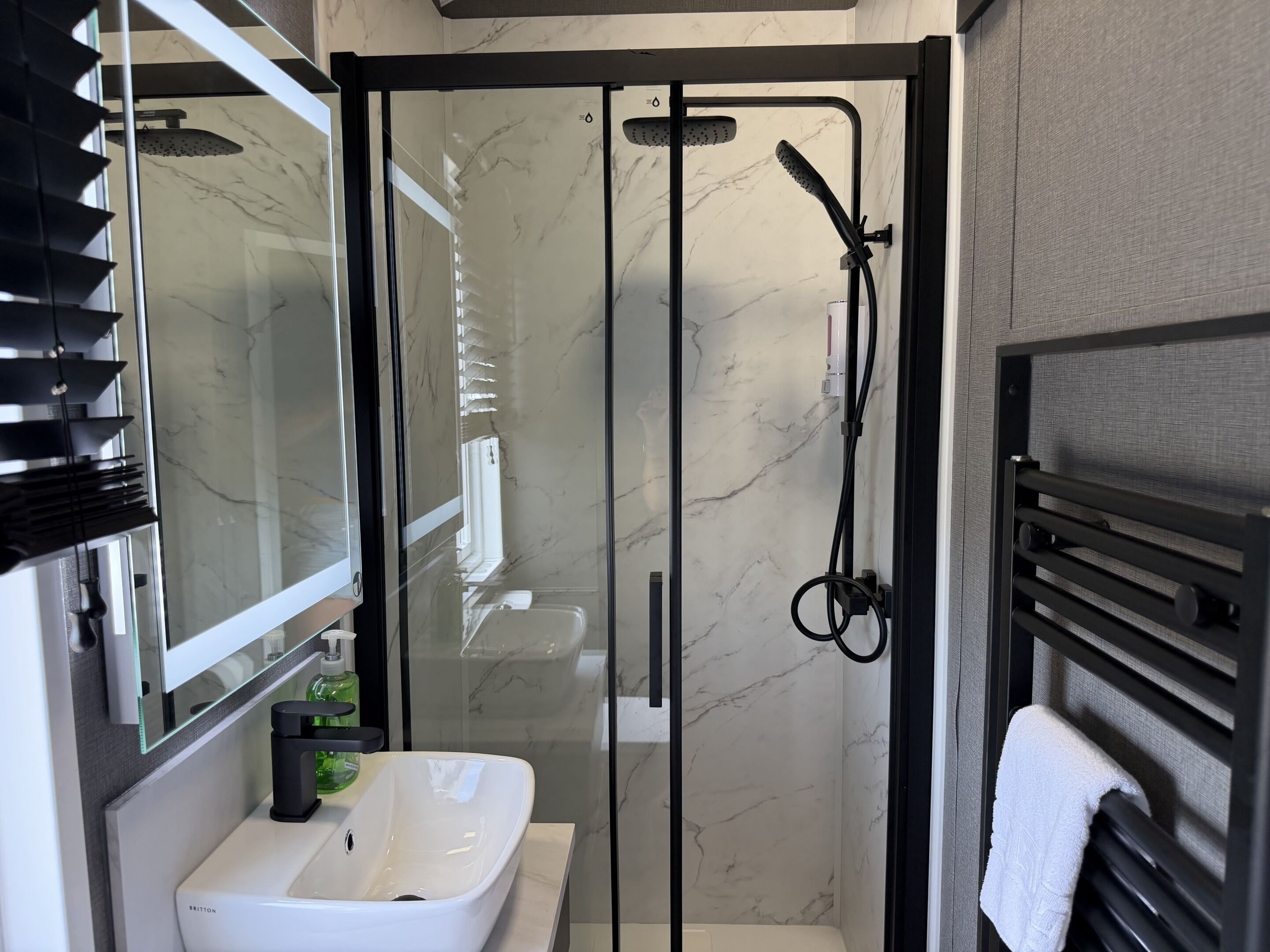 Un baño moderno con ducha envuelta en vidrio, un lavamanos blanco y un perchero para toallas.