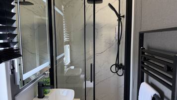 Un baño moderno con ducha envuelta en vidrio, un lavamanos blanco y un perchero para toallas.