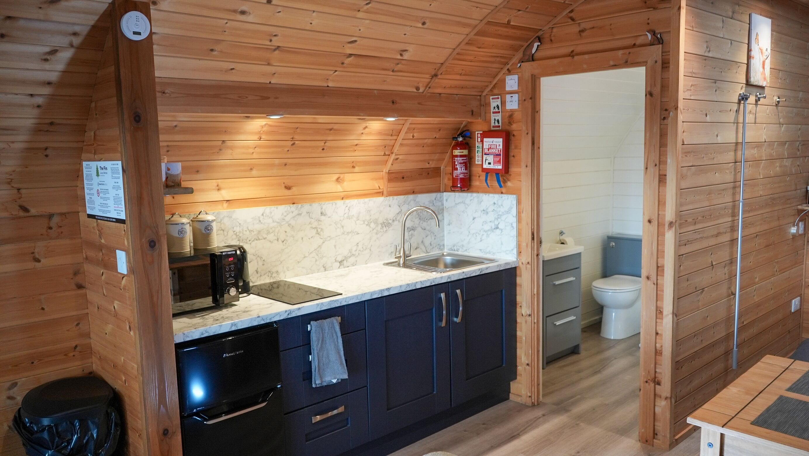 A compact kitchen with a sink, stove, and cabinets, leading to a bathroom with a toilet and shower.