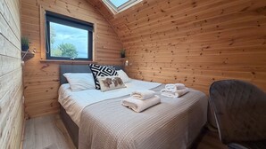 Un dormitorio rústico de madera con tragaluces, una cama con almohadas, una silla y toallas dobladas con esmero.