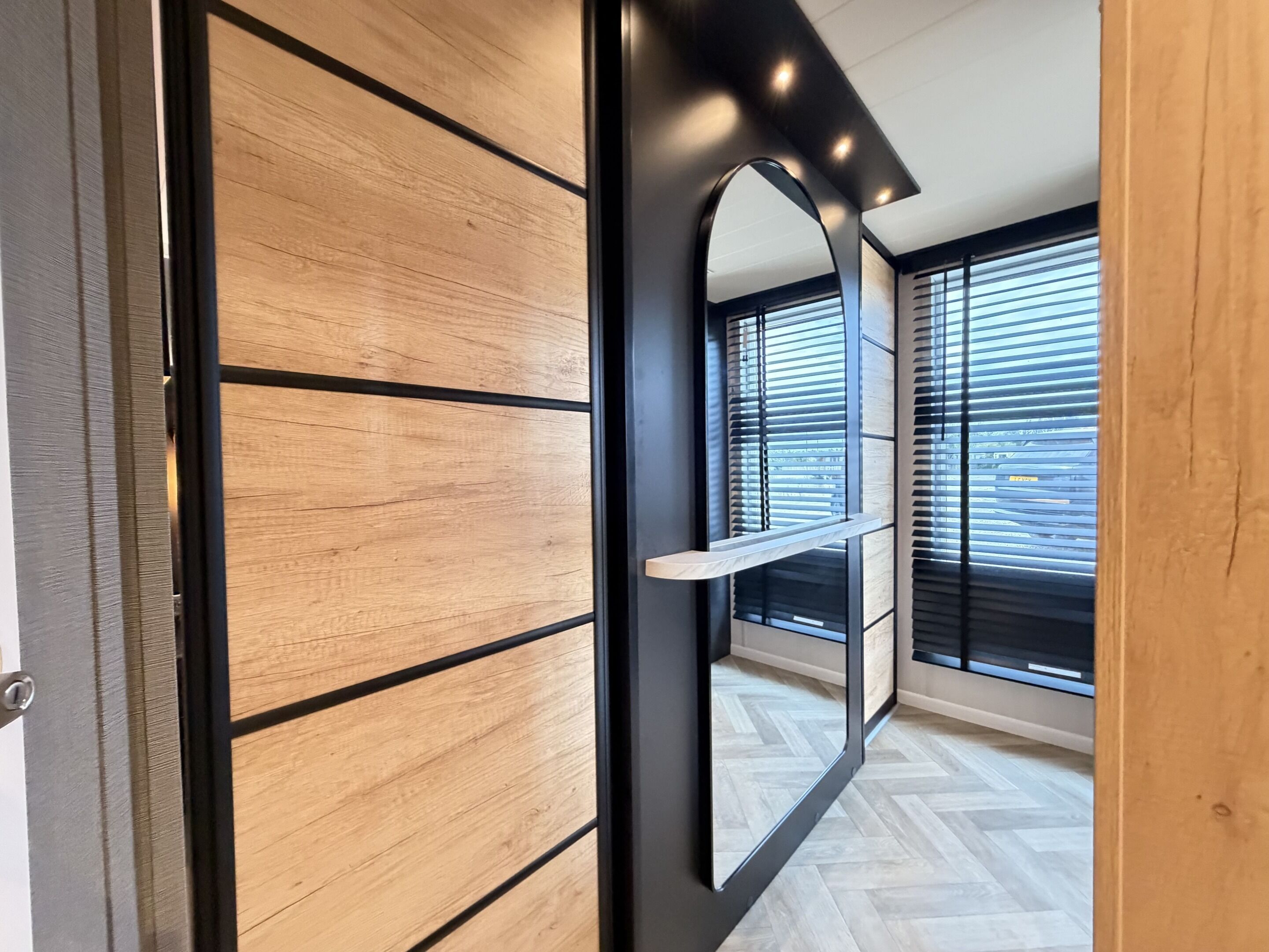 A modern interior with a wooden panel wall, a black-framed mirror, and a herringbone-patterned floor.